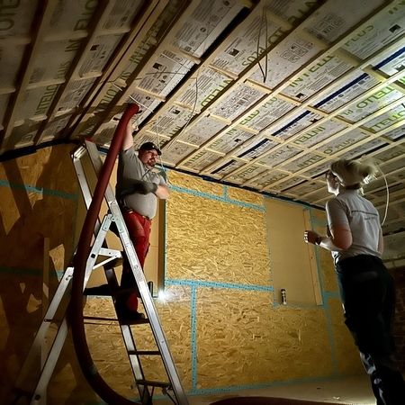 Mann steht auf einer Leiter und dämmt ein Dach via Einblasdämmung