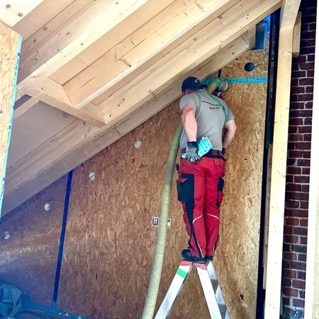 Mann steht auf einer Leiter und dämmt ein Dach via Einblasdämmung
